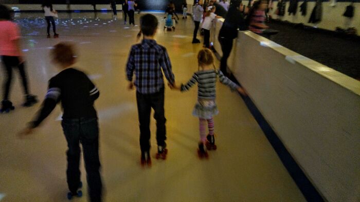 Three siblings roller skating together in a rink, enjoying a grateful and joyful moment of family bonding.
