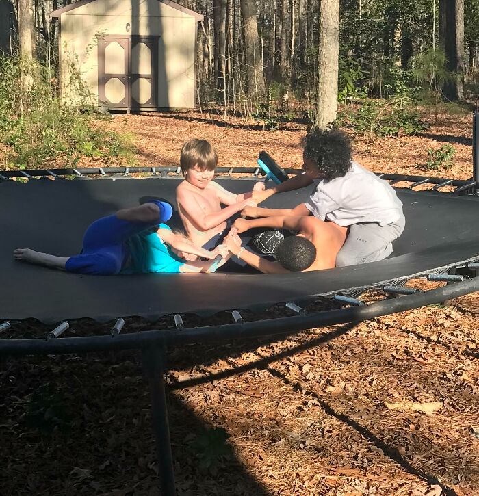 Three siblings play and laugh together on a trampoline in a sunny backyard, enjoying sibling gratitude and bonding.