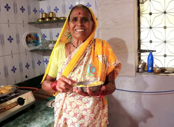 Smiling elderly woman in traditional attire holding a bowl of food in a kitchen, representing viral internet icons.
