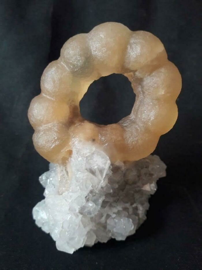 Unusual forbidden food resembling a translucent ring with bumpy texture resting on crystalline white base against black background.