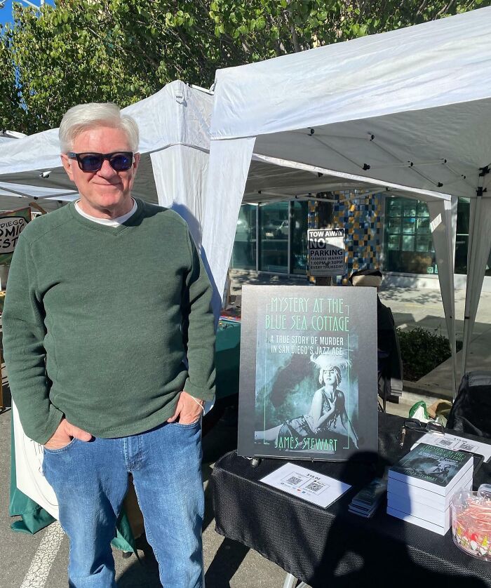 Man smiling outdoors at book fair, showcasing his book and turning his dreams into reality inspiring others online.