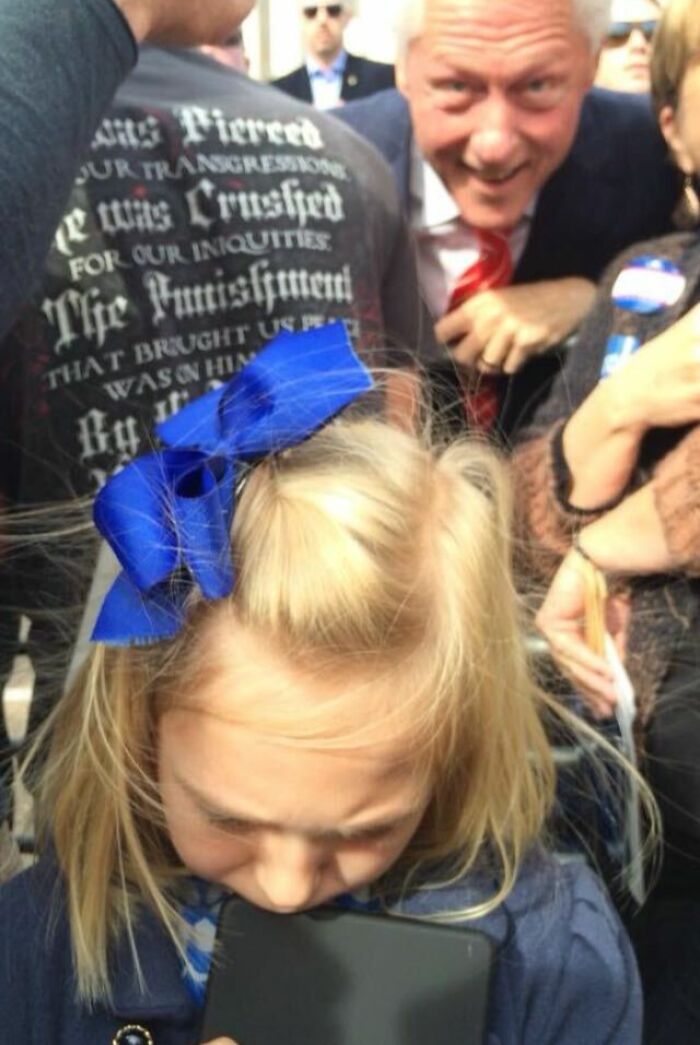 A man photobombs a candid shot of a young girl with a blue bow, creating an epic photobomb that steals the show.