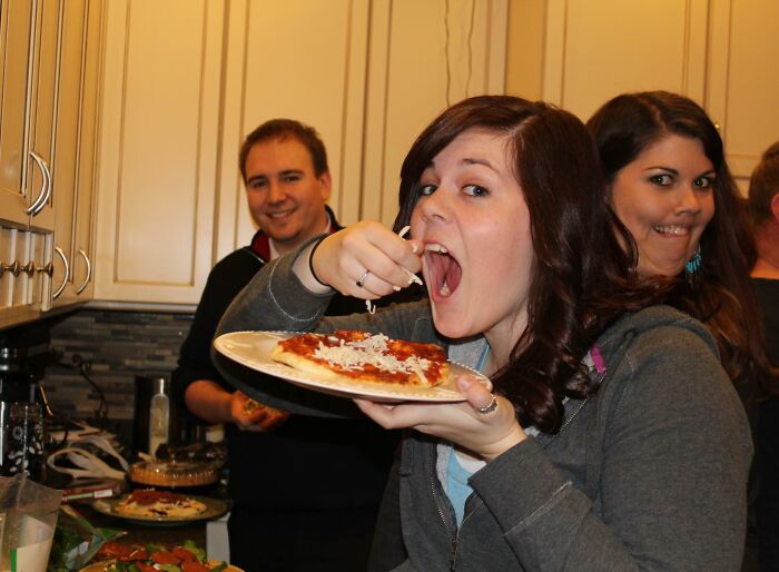 Woman eating pizza while a photobomb behind her makes a funny face, captured in an epic photobomb moment.