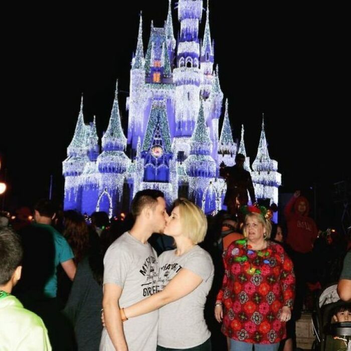 Couple kissing in front of a brightly lit castle with an epic photobomb stealing the show in the background.