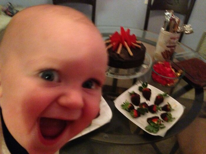 Close-up of a baby photobombing a party table with chocolate-covered strawberries and cake, creating an epic photobomb moment.
