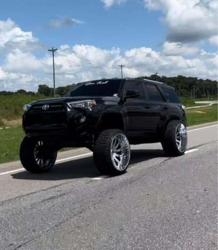 Black SUV with oversized custom rims and lifted suspension parked on a rural road showing car mods gone wrong.