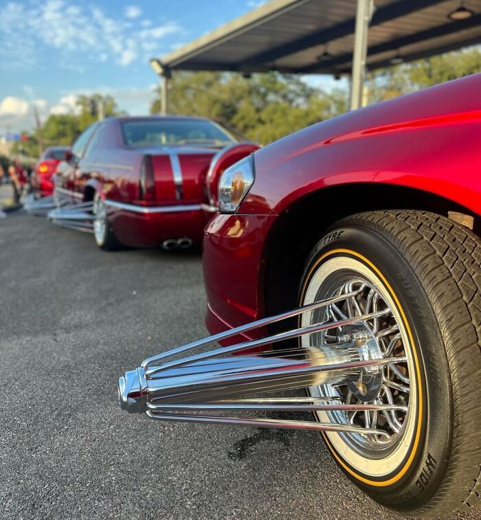 Red car with exaggerated chrome spoke wheel covers lined up with another customized vehicle, showcasing unusual car modifications.