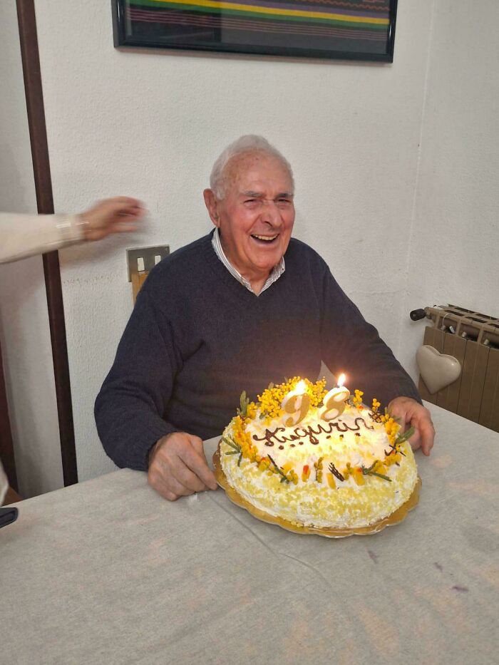 Elderly man smiling happily at birthday cake with candles, capturing wholesome internet moments of joy and celebration.