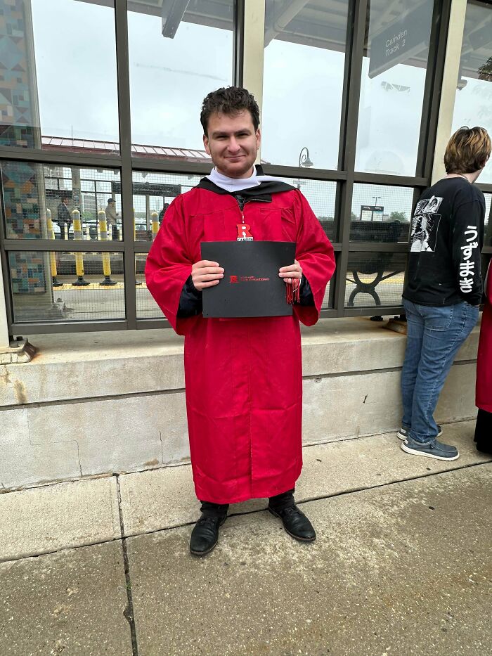 Graduate in red robe holding diploma, celebrating a wholesome internet moment of achievement and positivity online.