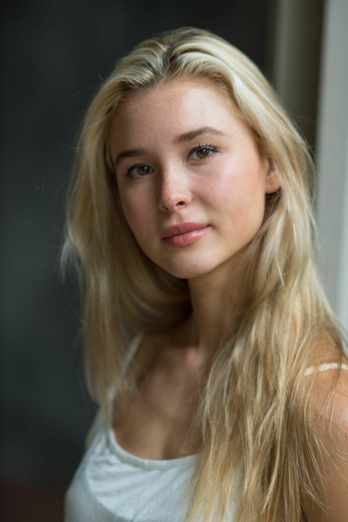 Isabel May with long blonde hair and natural makeup, posing indoors with soft natural light and neutral background