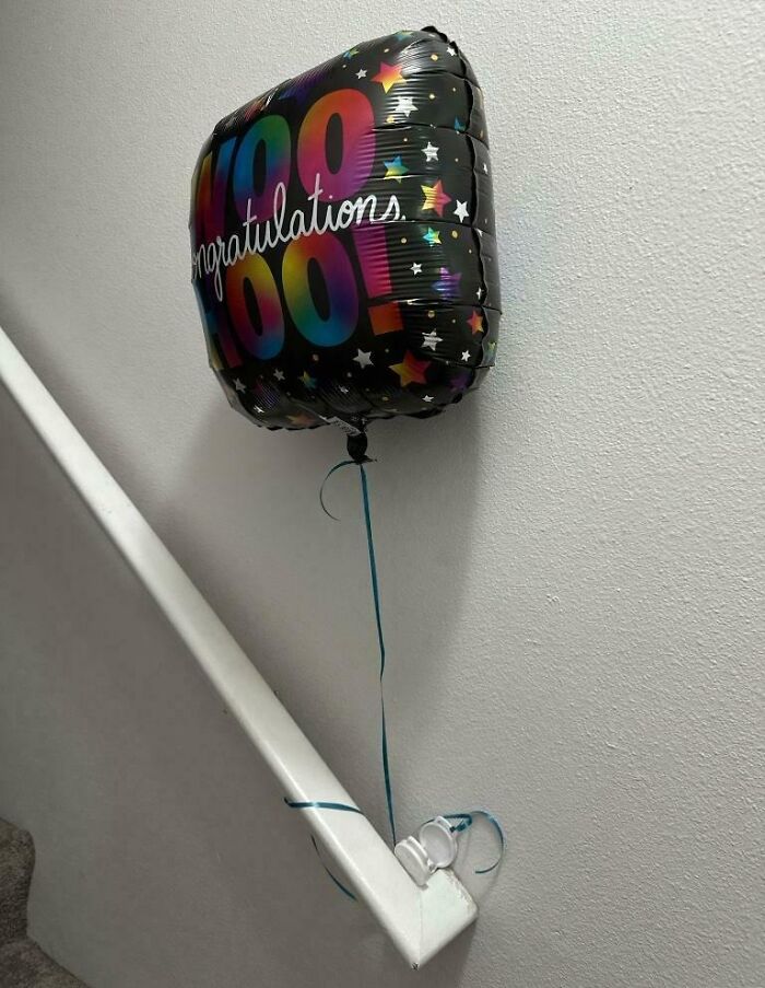 Colorful congratulations balloon tied to stair railing, a prank by employees with jokes and zero regrets at work.