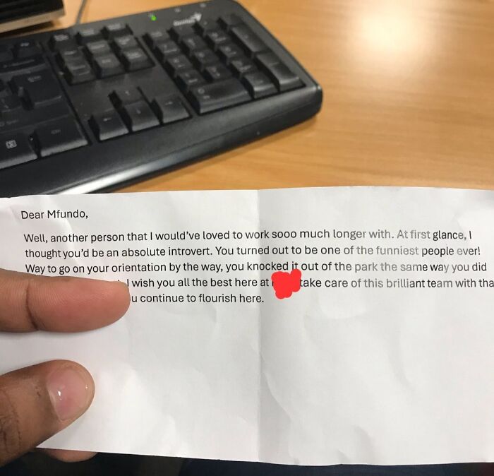 Hand holding a farewell note with jokes and pranks visible on a desk with a keyboard, highlighting employees humor.