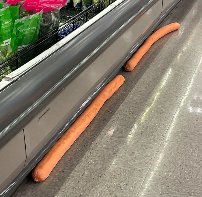 Two unusually long sausages placed on the floor inside a grocery store with salad bags nearby forbidden foods to resist eating.