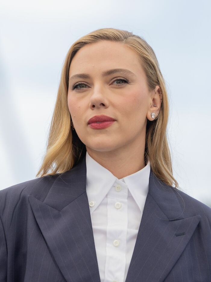 Scarlett Johansson wearing a navy blazer and white shirt, posing outdoors with a calm expression for a career highlights feature.