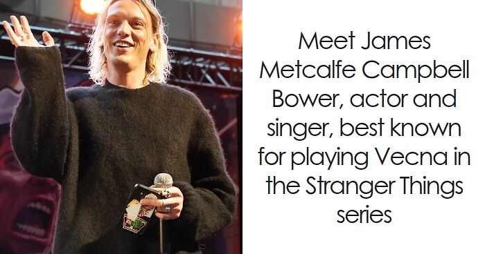 Jamie Campbell Bower speaking on stage, wearing a black sweater and holding a microphone during a public event.