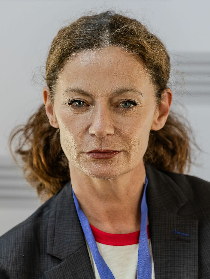 Michelle Gomez wearing a dark blazer and lanyard, looking directly at the camera in a neutral indoor setting.