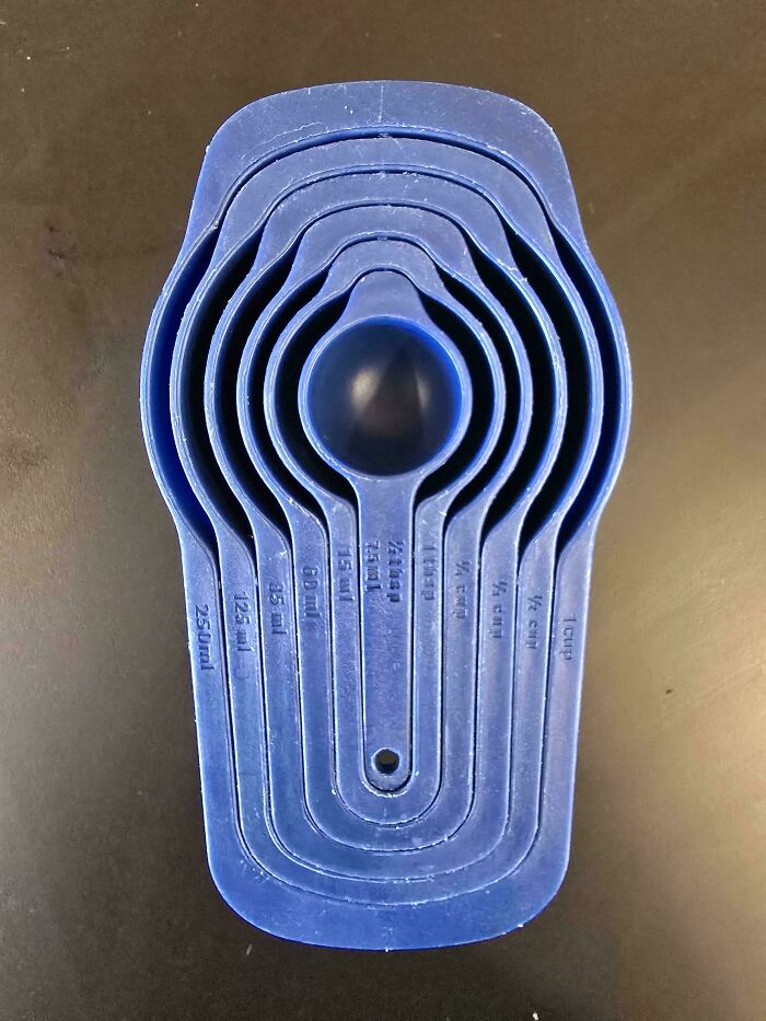Blue measuring spoons perfectly nested inside each other on a dark surface, showing precise alignment and shapes.
