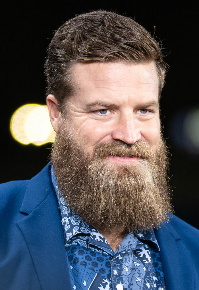Ryan Fitzpatrick with a full beard and styled hair wearing a patterned shirt and blue blazer in a close-up portrait.
