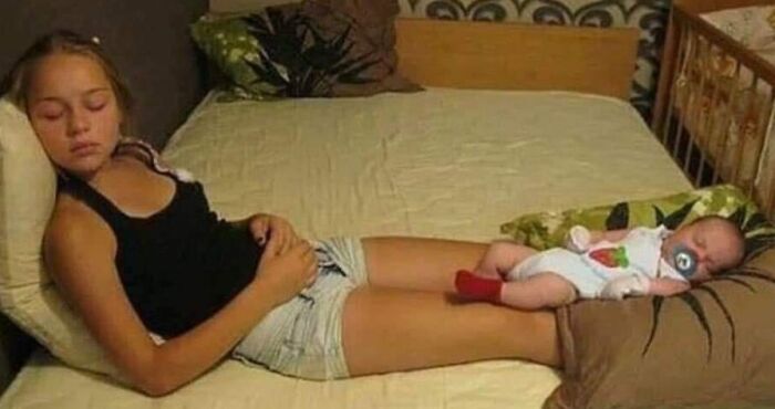 Young girl resting on a bed with a sleeping baby sibling lying on her legs, showing sibling gratitude and care.