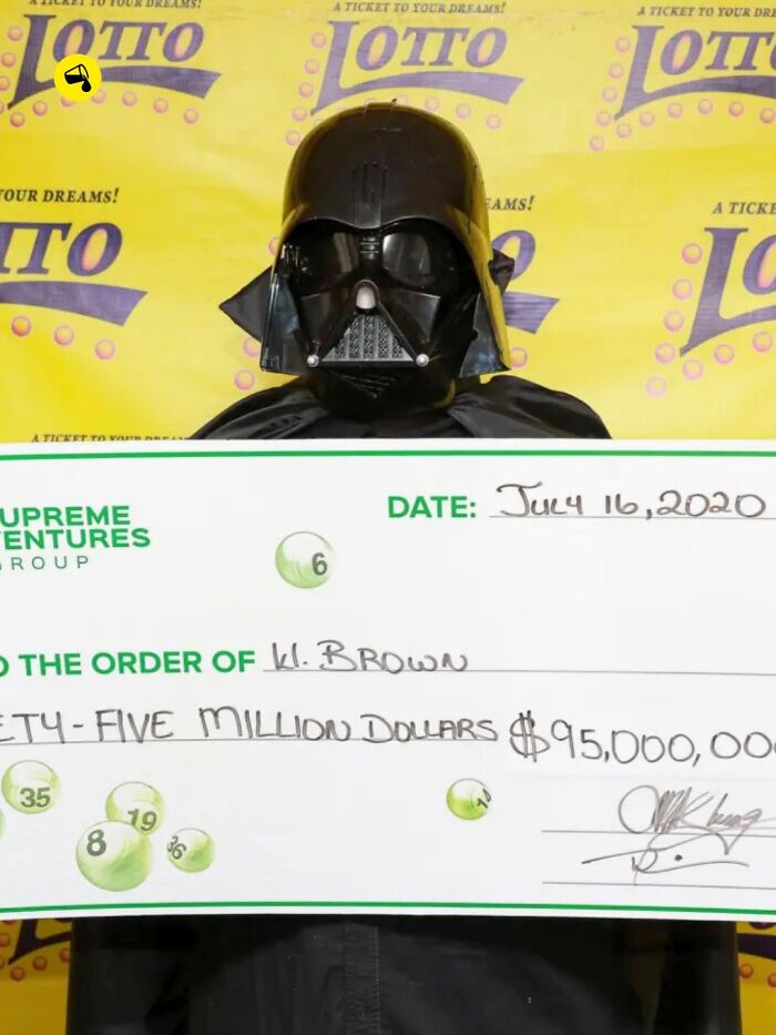 Person in dark helmet and cape holding large lottery check for 95 million, illustrating spill now facts and photos.