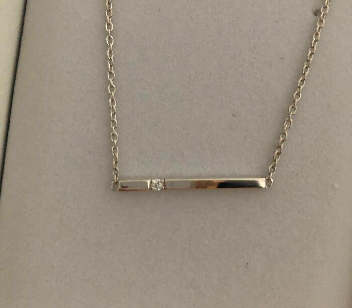 Delicate silver necklace with a horizontal bar pendant featuring a small embedded gem on a fine chain.