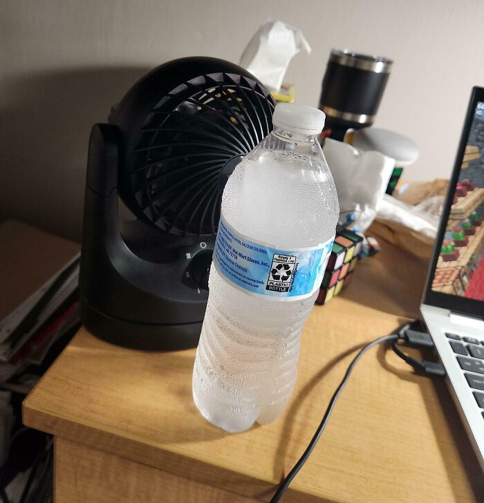Water bottle frozen and placed in front of small fan, showcasing inventive redneck engineer cooling hack on wooden desk.