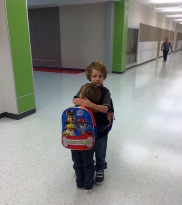 Two young siblings hugging tightly in a school hallway, showing gratitude and support for each other.