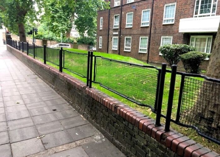 A low brick wall with oddly placed short black fences along a sidewalk in a strange urban setting.