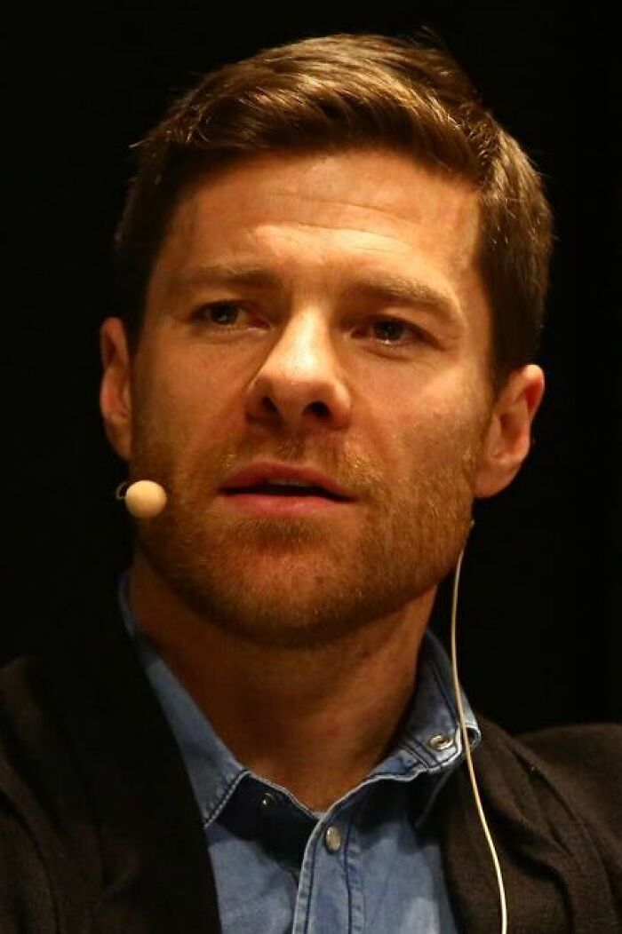 Xabi Alonso speaking with a headset microphone, wearing a blue shirt and black jacket during an event.
