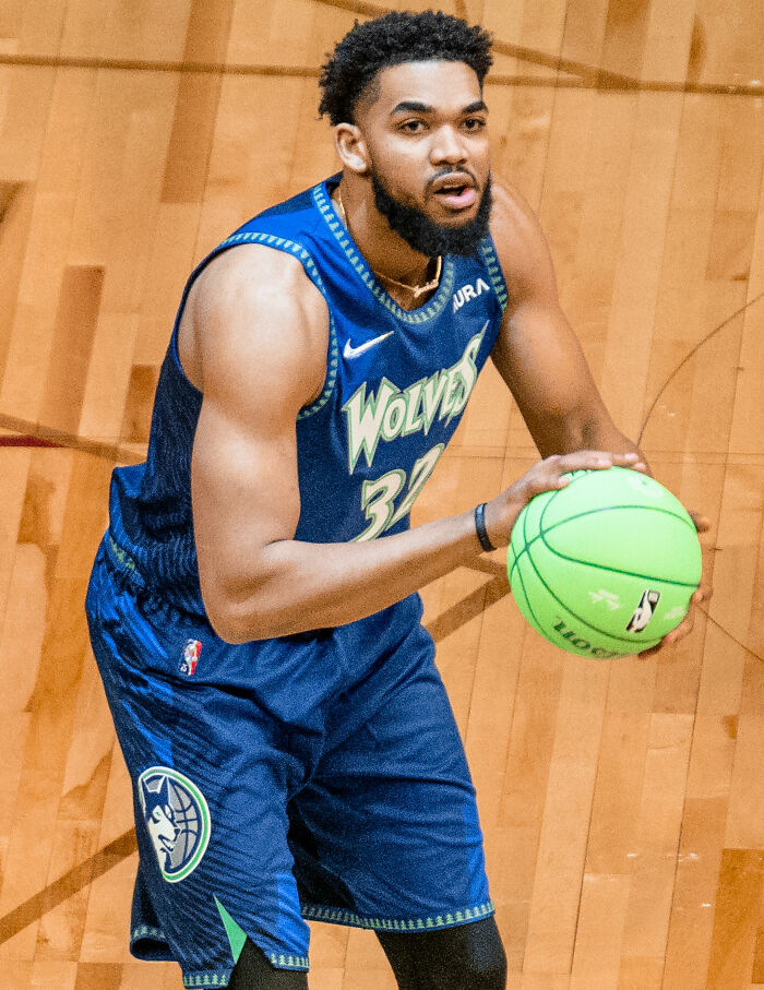 Karl-Anthony Towns in Wolves uniform holding a green basketball during a game on a wooden court.