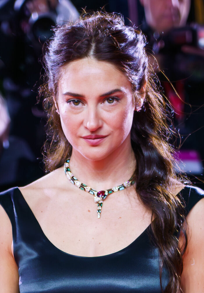 Shailene Woodley wearing a black dress and gemstone necklace at a red carpet event with photographers in the background