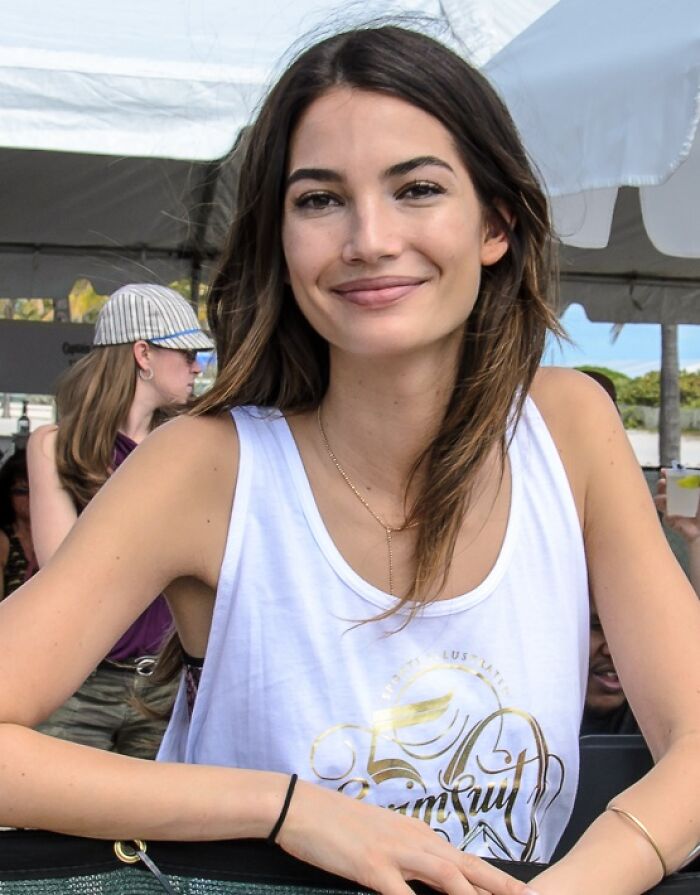 Lily Aldridge smiling outdoors at an event, wearing a white sleeveless top, showcasing her bio and career highlights.