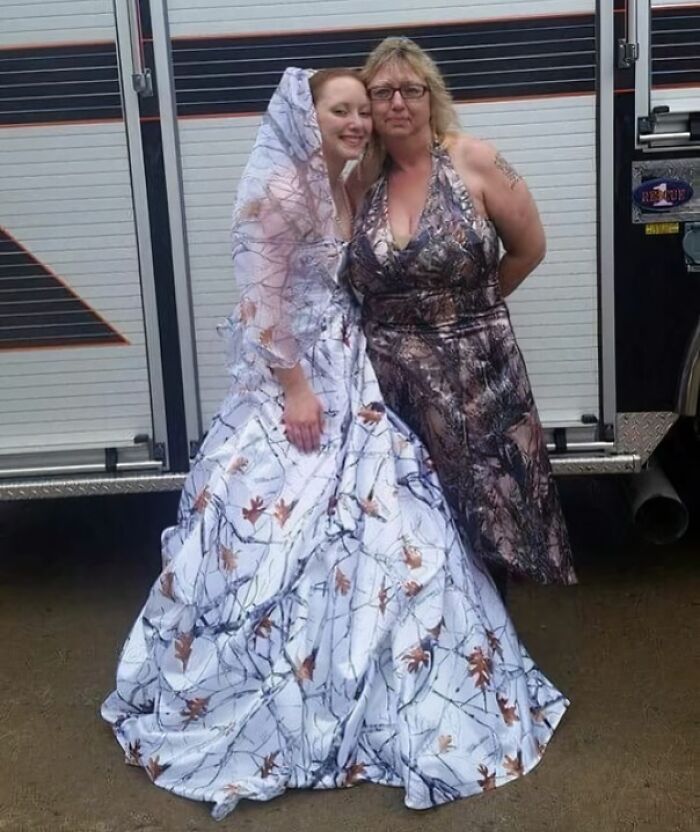 Bride and woman in unusual patterned wedding dresses standing outdoors in front of a vehicle, showcasing questionable taste.
