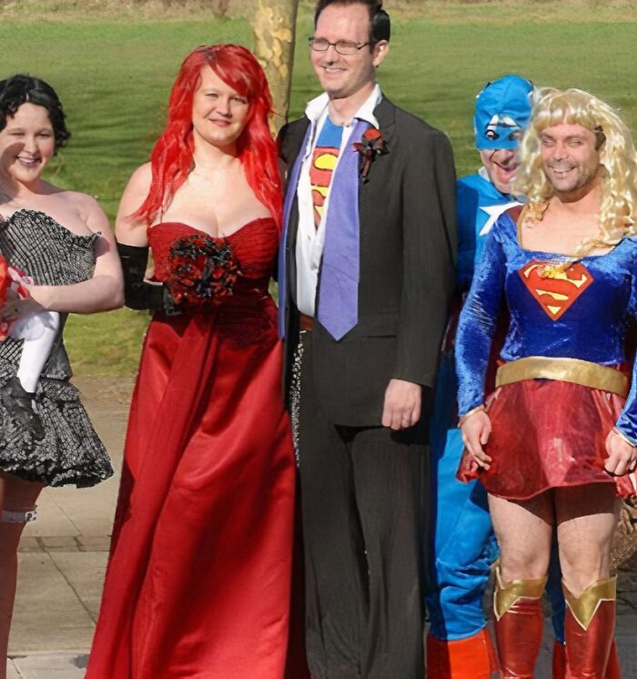 Group of people in questionable wedding dresses and superhero costumes posing outdoors on a sunny day.