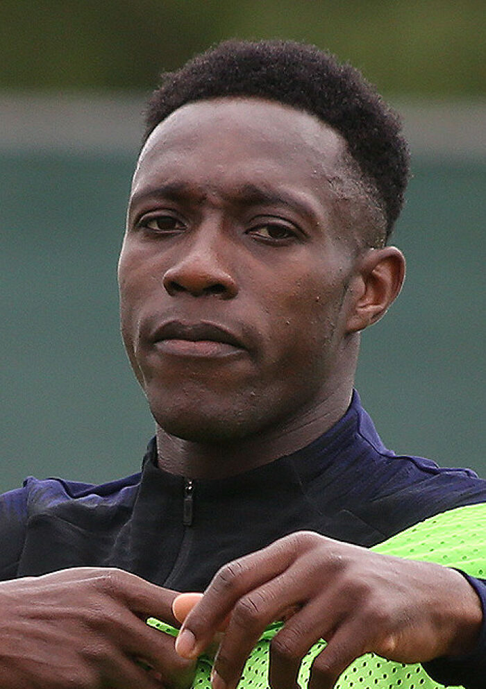 Danny Welbeck focused outdoors, adjusting sportswear during training session on a green field background.