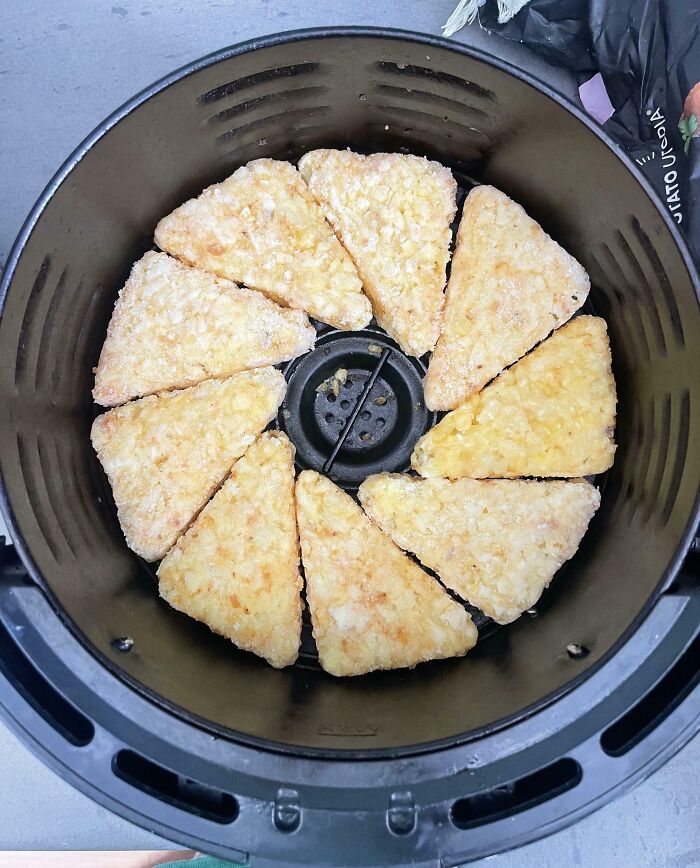 Perfectly aligned frozen hash brown triangles neatly arranged in a circular pattern inside an air fryer basket