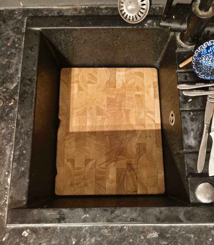 Wooden cutting board perfectly aligned inside a black kitchen sink, demonstrating things aligned perfectly for satisfying effect.