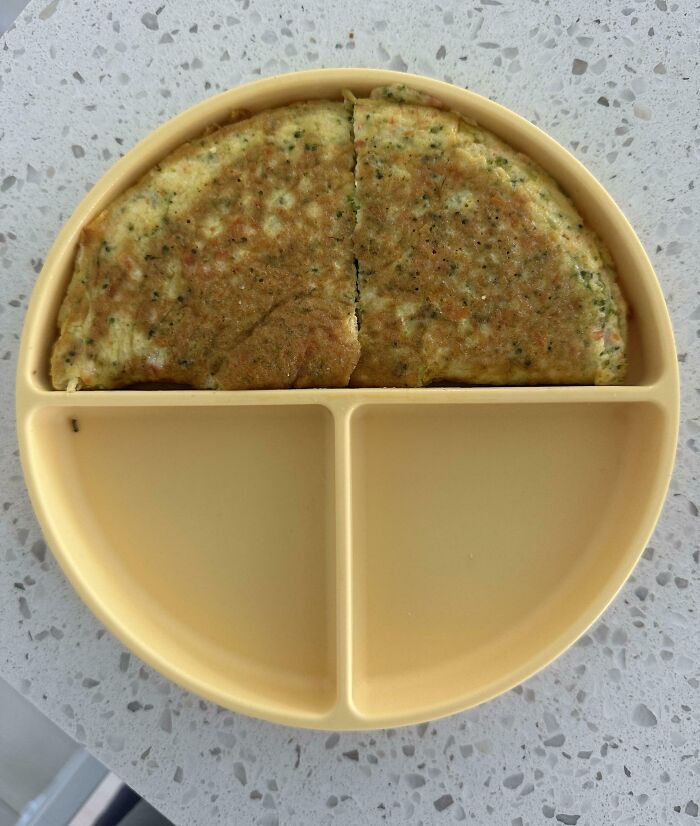 Yellow divided plate holding a folded omelette perfectly aligned with the plate’s semicircular section on a speckled counter.