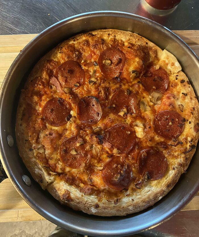 Pepperoni slices perfectly aligned on a freshly baked pizza in a round metal pan on a wooden surface.
