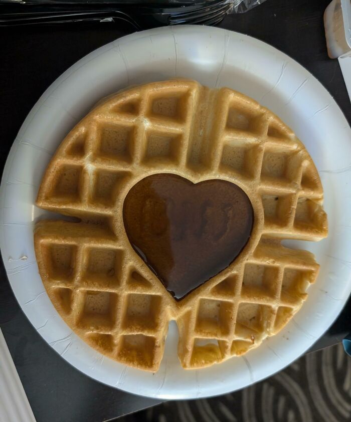 Heart-shaped syrup perfectly aligned in the center of a round waffle on a white paper plate, showcasing perfect alignment.