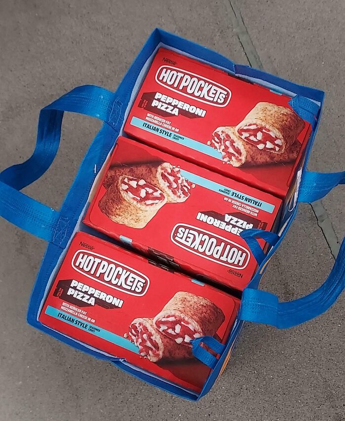 Three Hot Pockets boxes perfectly aligned inside a blue reusable shopping bag on a concrete surface.