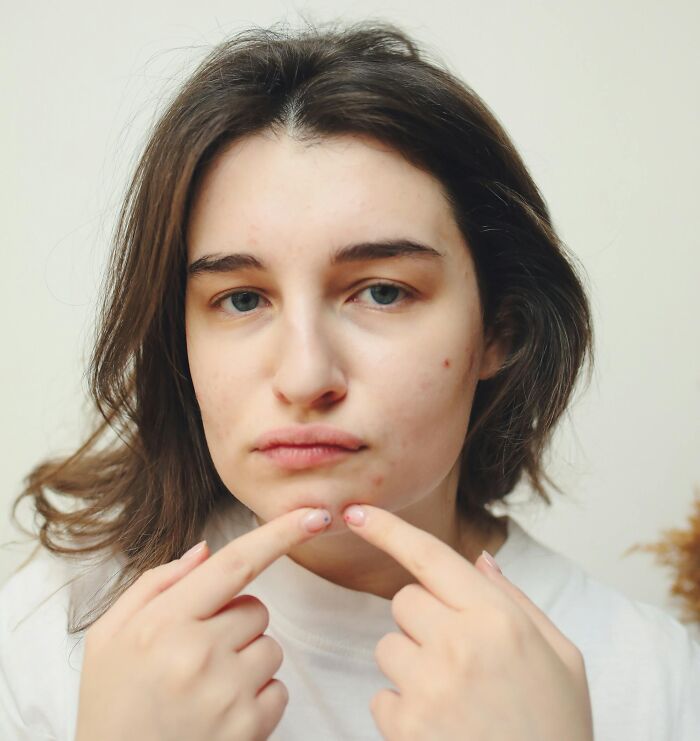 Young woman examining her skin closely, relatable to guilty habits and ridiculous but common personal care actions.