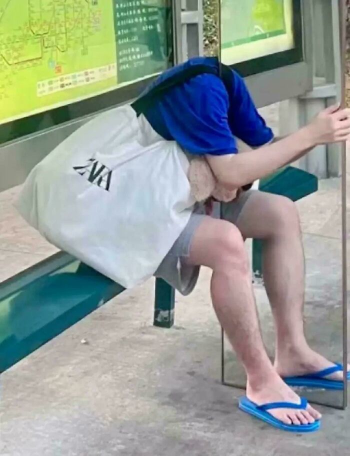 Person sitting on a bench with a shirt covering their head, holding a mirror that creates a confusing visual effect.