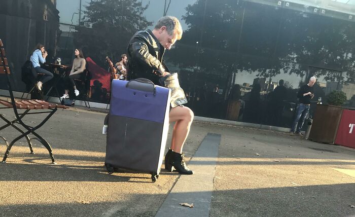 Person sitting on a suitcase in an outdoor area, creating a confusing visual that tricks the brain momentarily.