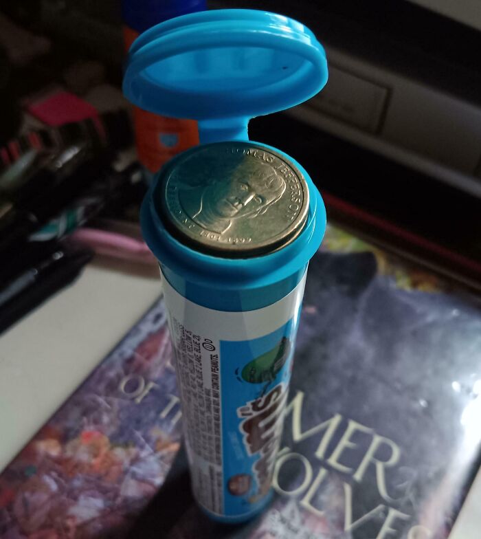 Coin perfectly aligned on the opened cap of a blue cylindrical container, demonstrating perfect alignment.
