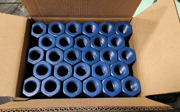 Box of blue hex nuts aligned perfectly inside a cardboard box, showcasing precise and satisfying arrangement.