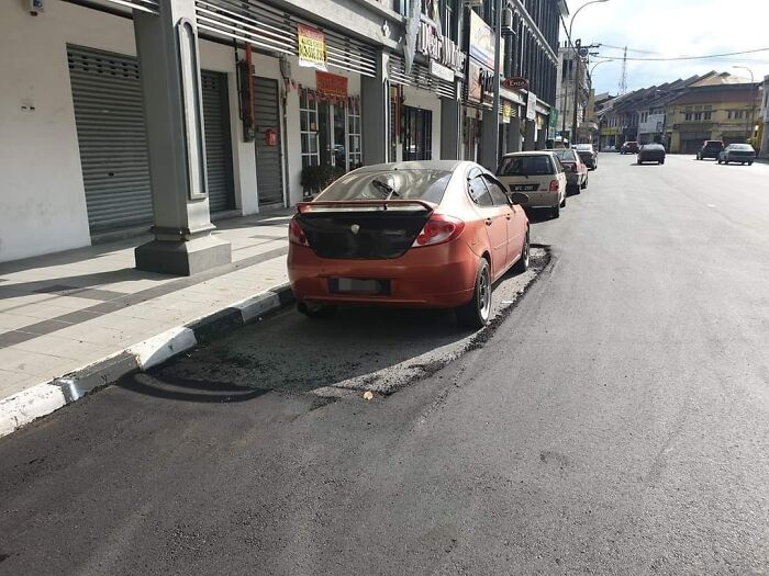 Car parked in a spot with freshly laid asphalt that poorly fits the space, showing job done almost impressively wrong