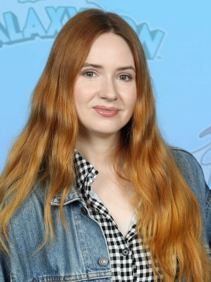 Karen Gillan with long red hair wearing a denim jacket and checkered shirt at a promotional event.