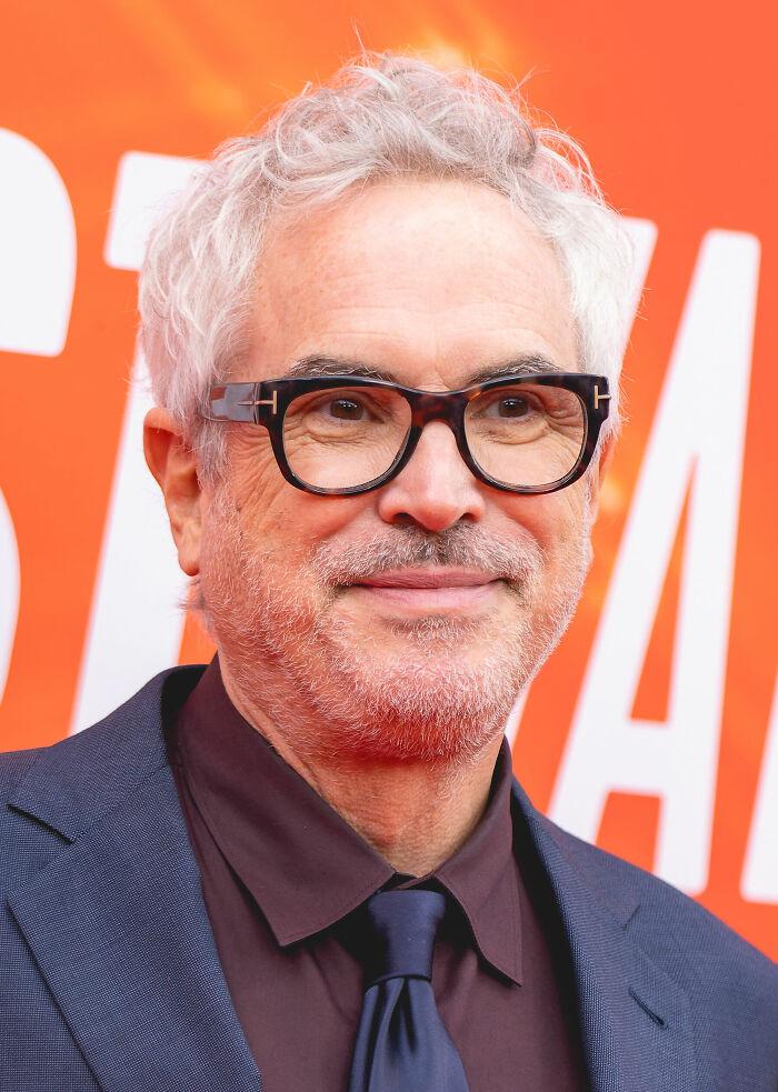 Alfonso Cuarón wearing glasses and a suit at a film event, showcasing his career highlights and presence.