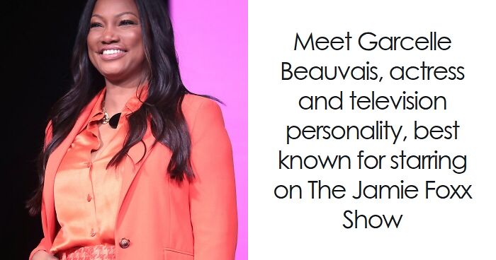 Garcelle Beauvais smiling in a coral blazer and shirt, known for her career in acting and television.